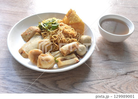 dry yellow egg noodles dory fish and fishball with bean sprout topping crispy dumpling on plate with soup 129989001