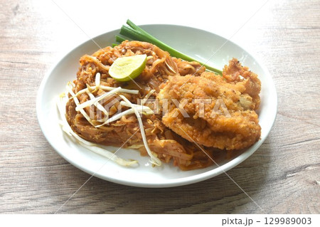 Pad Thai stir fried rice noodles with dry shrimp and egg topping crispy fried chicken on plate  129989003