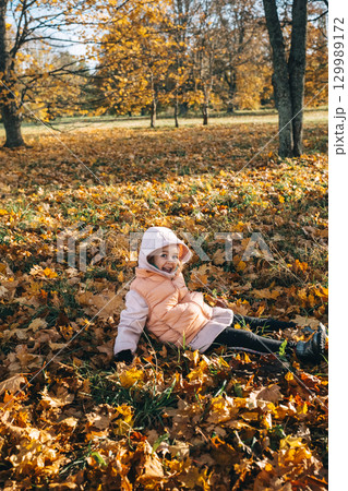 Little girl enjoying autumn in a park lying on fall foliage on a sunny day 129989172
