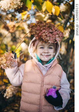 Little girl enjoying autumn in a park while holding colorful foliage on a sunny day 129989173