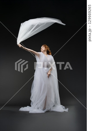 Elegant bride in sheer lingerie embracing a flowing veil in dramatic light 129989265