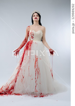 Stunning bride in elegant gown covered in blood stands with a knife Stunning bride in elegant gown covered in blood stands with a knife 129989282