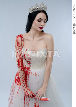 Bride in bloodied lingerie holding a knife in a hauntingly beautiful pose 129989286