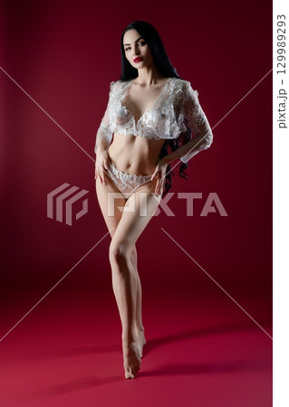 Elegant bride in delicate lingerie poses against deep red backdrop Elegant bride in delicate lingerie poses against deep red backdrop 129989293