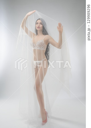 Beautiful bride in delicate lingerie poses with soft veil 129989296