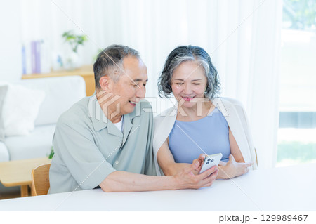リビングでスマホを見るシニア夫婦 リビングでスマホを見るシニア夫婦 129989467
