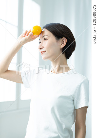 レモンを手に持って額にかざす透明感のある女性 顔のアップ レモンを手に持って額にかざす透明感のある女性 顔のアップ 129989675