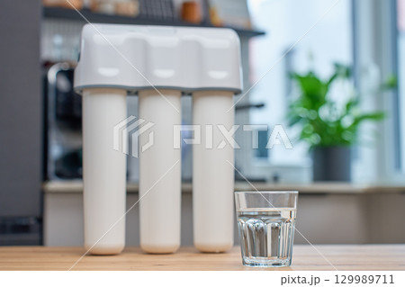 Glass of filtered drinking water and water filtration system on kitchen table Glass of filtered drinking water and water filtration system on kitchen table 129989711