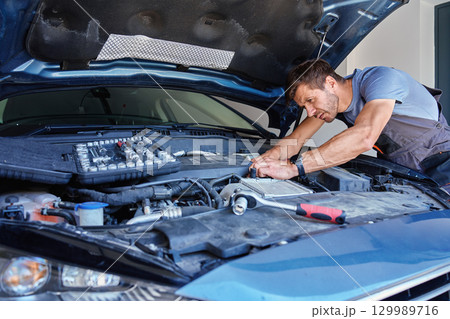 Mechanic holding wrench over car engine during repair 129989716