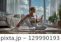 Woman stretching at home in sportswear while checking smartphone in sunny room 129990193