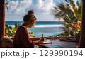 Woman writing in notebook at tropical seaside desk surrounded by palm trees 129990194