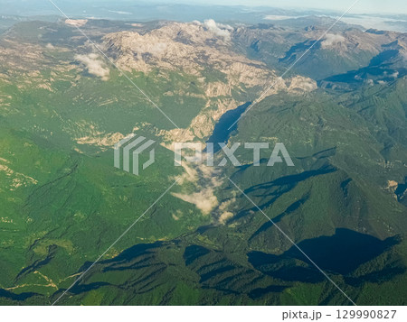 Aerial view of lush mountain valley with scattered clouds. Natural relief, light and shadow play, and dramatic terrain from above. Aerial view of lush mountain valley with scattered clouds. Natural relief, light and shadow play, and dramatic terrain from above. 129990827