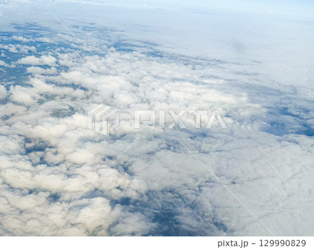 Cloudy aerial view with distant industrial chimney. Weather formation, aerial visibility, and atmospheric depth from airplane flight. Cloudy aerial view with distant industrial chimney. Weather formation, aerial visibility, and atmospheric depth from airplane flight. 129990829