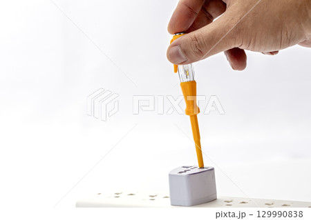 Hand using tester screwdriver on power strip socket electrical safety check white background close up precaution home maintenance risk awareness careful action indoor adult hand Hand using tester screwdriver on power strip socket electrical safety check white background close up precaution home maintenance risk awareness careful action indoor adult hand 129990838