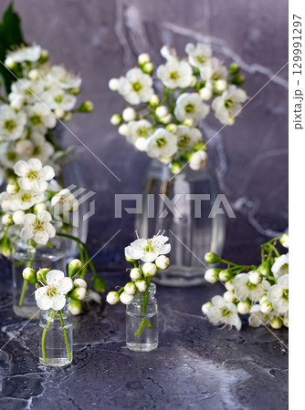 Beautiful white flowers arranged in small glass vases on a wooden table, showcasing a fresh and natural aesthetic in a bright indoor space Beautiful white flowers arranged in small glass vases on a wooden table, showcasing a fresh and natural aesthetic in a bright indoor space 129991297