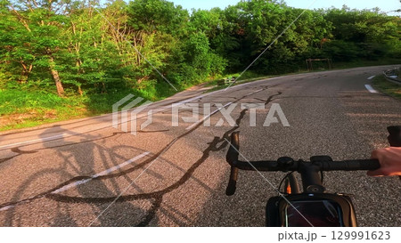 Point of view shot of a road cyclist riding along a winding asphalt road with visible shadow on the ground during sunrise Point of view shot of a road cyclist riding along a winding asphalt road with visible shadow on the ground during sunrise 129991623
