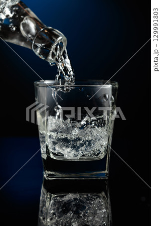 Crystal clear vodka being poured over ice in a glass. 129991803