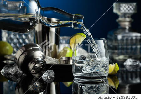 Vodka is poured into a glass with ice. Vodka is poured into a glass with ice. 129991805