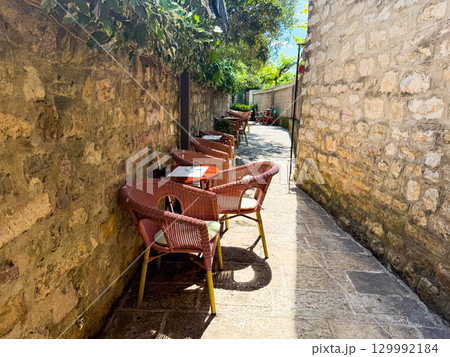 Outdoor cafe chairs along a narrow stone alley. Travel, leisure, lifestyle and relaxation in a historic European setting. 129992184