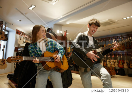 In a music store, a man and a woman are playing their guitars skillfully 129994559