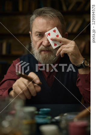A focused gentleman with a groomed beard holds a playing card 129994578