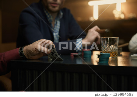 Poker game featuring cigars and assorted drinks on the table Poker game featuring cigars and assorted drinks on the table 129994588