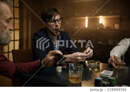 A group of men enjoying time playing cards in a dimly lit bar while sipping on drinks A group of men enjoying time playing cards in a dimly lit bar while sipping on drinks 129994591