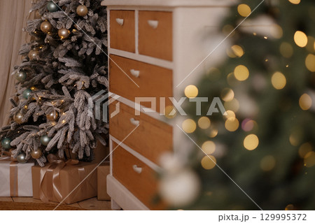 Decorated Christmas tree with gifts near wooden dresser in cozy room 129995372
