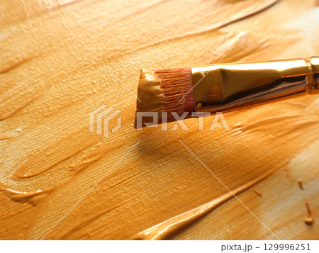 Close-Up of Gold Paint on Brush and Canvas in Artistic Setting 129996251