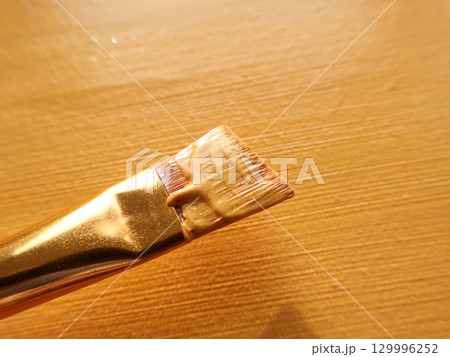 Close-Up of Paintbrush With Gold Tone Handle on Wooden Surface Close-Up of Paintbrush With Gold Tone Handle on Wooden Surface 129996252