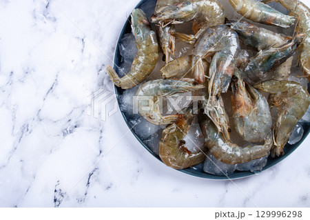 Fresh raw shrimp spread on ice with lemon and cilantro slices on a marble surface, ready to cook, no people Fresh raw shrimp spread on ice with lemon and cilantro slices on a marble surface, ready to cook, no people 129996298