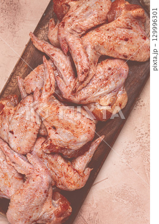 Chicken wings, marinated and laid out on a wooden platter, ready for cooking, grilling or baking, in a home kitchen, there are no people Chicken wings, marinated and laid out on a wooden platter, ready for cooking, grilling or baking, in a home kitchen, there are no people 129996301