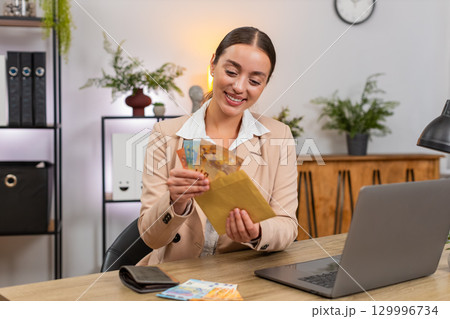 Young businesswoman counts euro cash from wallet plans budget and puts part into reserve envelope 129996734