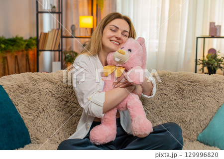 Woman hugging plush toy at home smiling with comfort and calmness feeling safe emotionally grounded 129996820