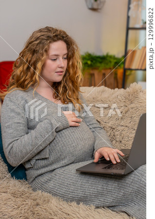 Pregnant woman browsing baby products on laptop, smiling with excitement emotional anticipation 129996822