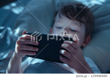 Child Watching Smartphone Screen in Bed at Night 129996980