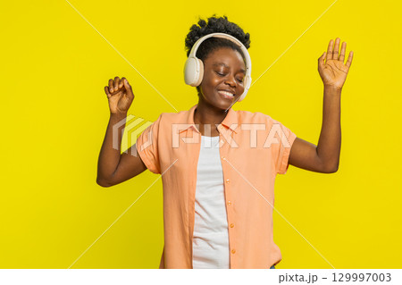 Happy Black young woman listening music on headphones and dancing disco fooling around having fun 129997003