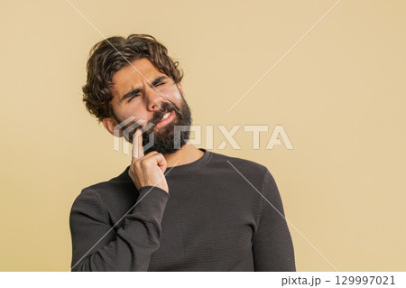 Young Indian bearded man touching sore cheek suffering from toothache cavities on beige background Young Indian bearded man touching sore cheek suffering from toothache cavities on beige background 129997021
