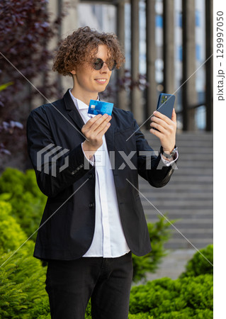Happy businessman using smartphone and credit card for online shopping standing on city street Happy businessman using smartphone and credit card for online shopping standing on city street 129997050