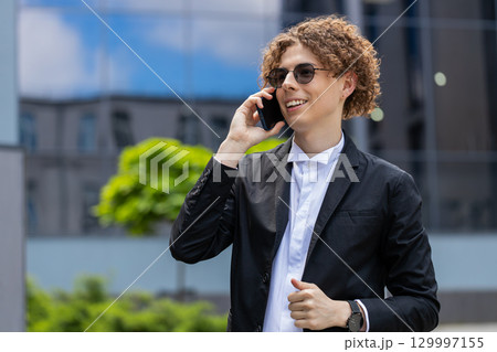 Businessman making phone call online conversation loudspeaker talking waving hello outside office 129997155