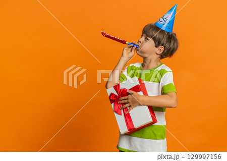 Happy excited lucky boy wearing birthday hat cone blow pipe celebrating party success win victory 129997156