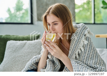 Young woman under blanket with cup with lemon, at home on sofa Young woman under blanket with cup with lemon, at home on sofa 129997197