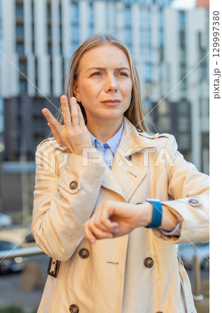 Serious sad mature businesswoman standing outdoors looking around waiting for business meeting 129997380