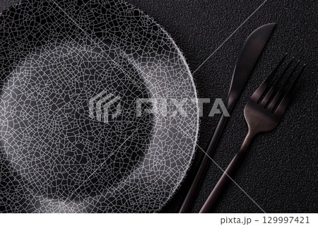 Empty round black plate for food, kitchen utensils on dining table. Empty plate 129997421