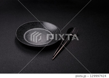 Empty round black plate for food, kitchen utensils on dining table. Empty plate Empty round black plate for food, kitchen utensils on dining table. Empty plate 129997424