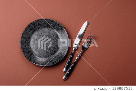 Empty round black plate for food, kitchen utensils on dining table. Empty plate 129997513
