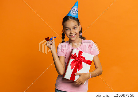 Happy excited lucky girl wearing birthday hat cone blow pipe celebrating party success win victory Happy excited lucky girl wearing birthday hat cone blow pipe celebrating party success win victory 129997559
