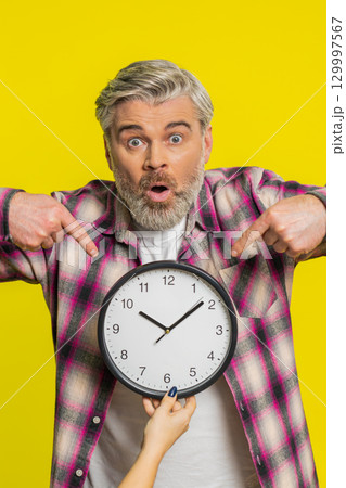 Mature man holding big office clock, urgent deadline sign, anxious lateness gesture time pressure Mature man holding big office clock, urgent deadline sign, anxious lateness gesture time pressure 129997567