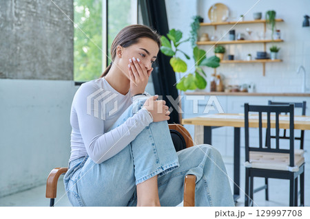 Sad upset teenager girl sitting at home in living room 129997708