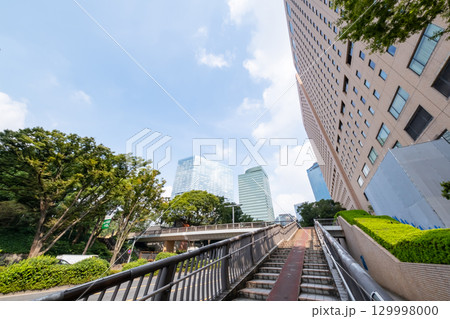 街路樹と高層ビルと歩道橋を見上げるオフィス街の風景 129998000